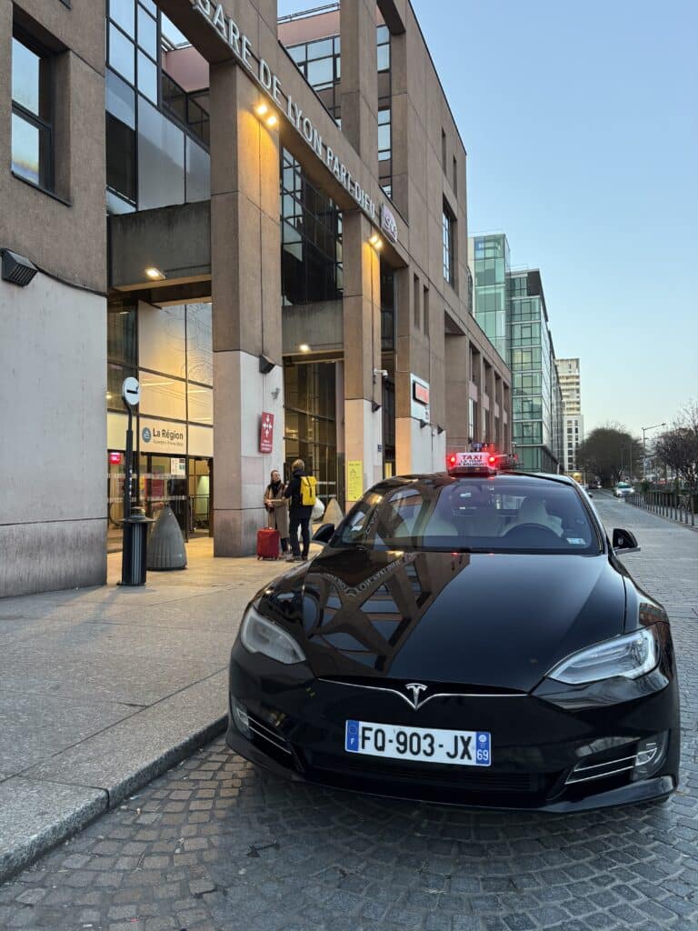 Taxi Tesla Model S devant la Gare Lyon Part-Dieu Taxi Tesla Model S noir devant la Gare de Lyon Part-Dieu, avec enseigne Taxi La Tour de Salvagny et voyageurs.